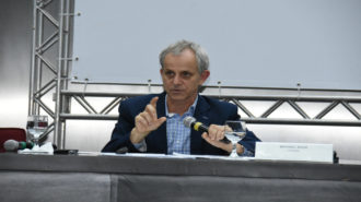 Foto do palestrante Michael Bach falando ao microfone, na mesa.