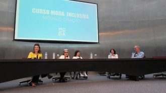 Foto palco do auditório da Secretaria de Estado dos Direitos da Pessoa com Deficiência. Na mesa, a Secretária Célia Leão, a Consultora de Moda Costanza Pascolato e dois professores.